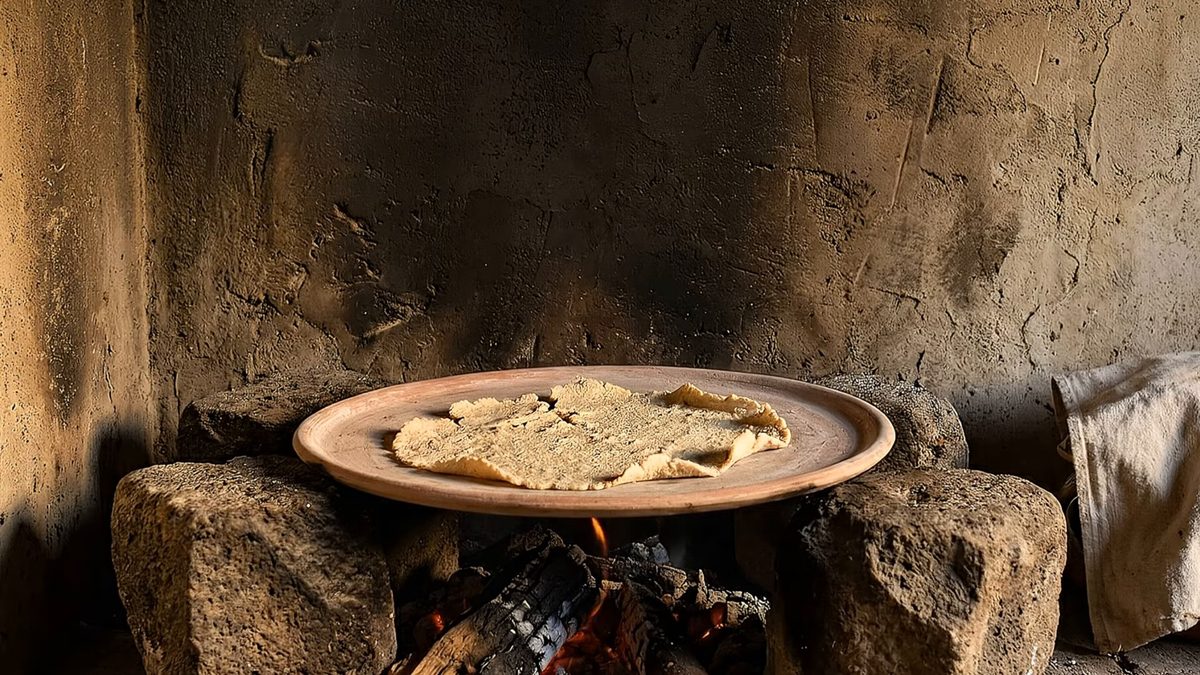 Comal de barro sobre un fogón de piedra encendido, con tortillas rotas encima.