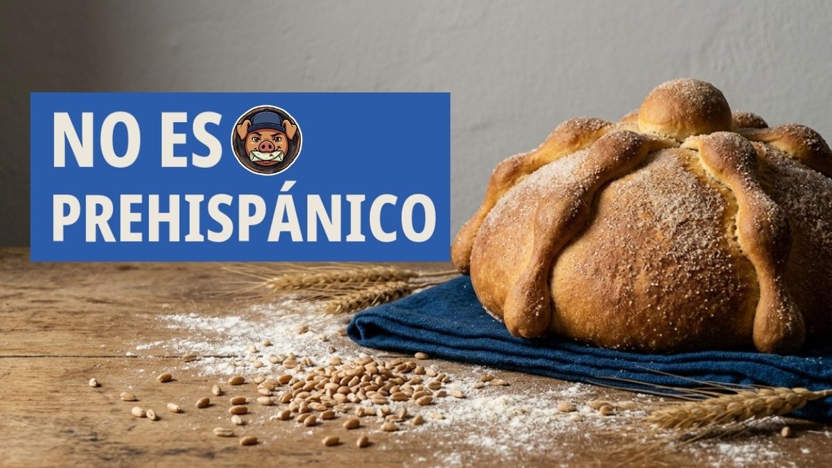 Pan de muerto espolvoreado de azúcar, con sus tiras y su bolita, sobre un paño azul, con harina, granos y espigas de trigo.