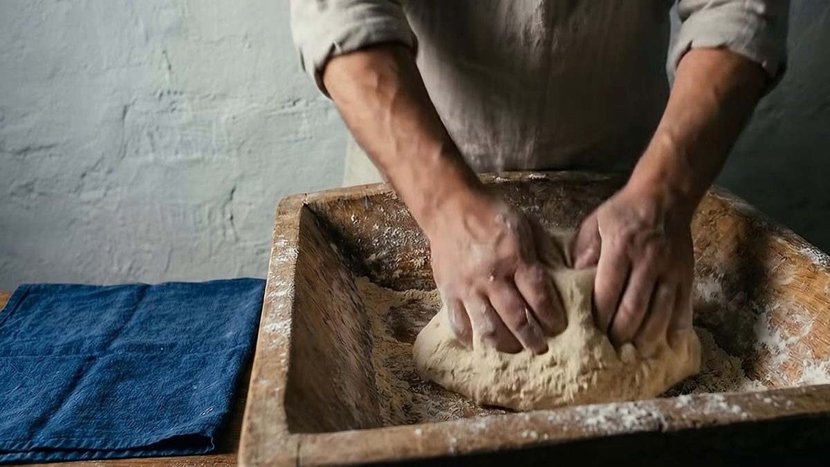 Dos manos amasan dentro de una batea de madera enharinada.
