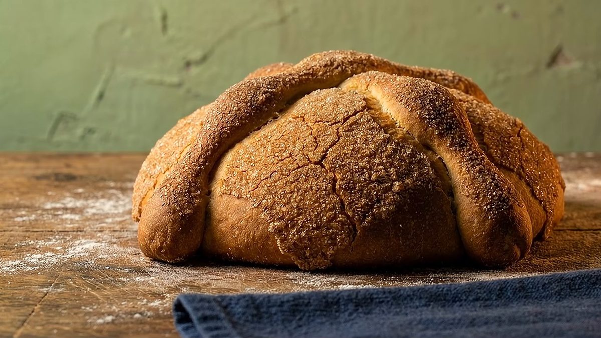 Pan de muerto horneado y cubierto de azúcar sobre una mesa enharinada.